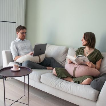 para ludzi siedząca na jasnej kanapie w przytulnym pokoju, na kolanach trzymają poduszki do relaksacji w kształcie księżyca